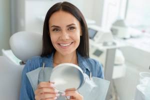a smiling female dental patient holds a mirror