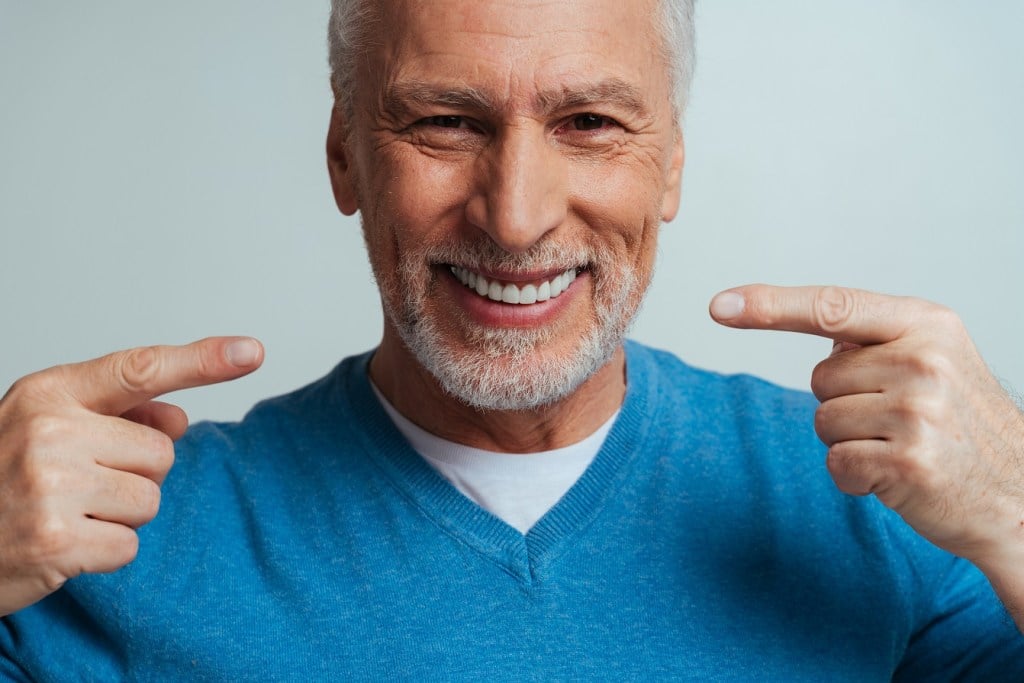 an older man points at his smile