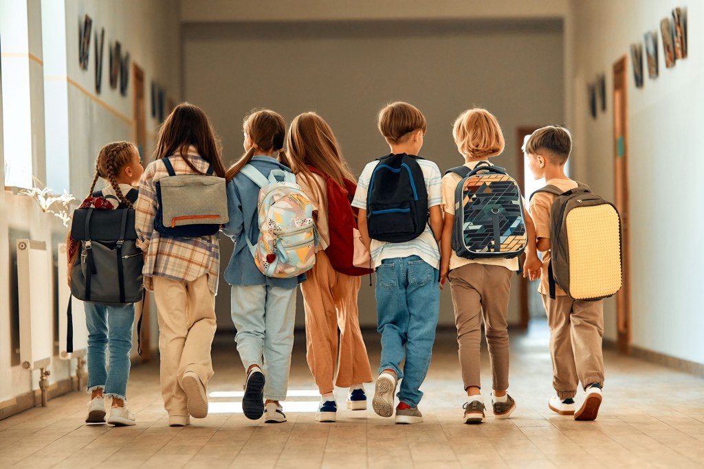 group of elementary students with backpacks walking in hallway